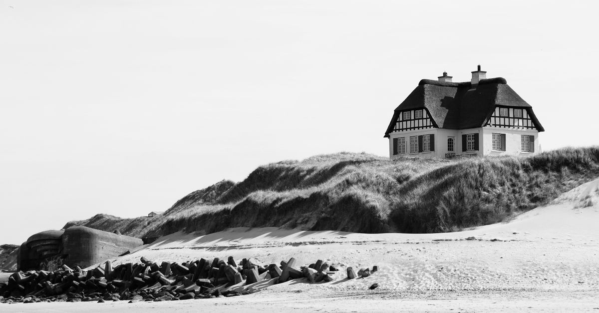 A quaint beach house on Dänemark dunes, showcasing classic architecture with a serene coastal backdrop.